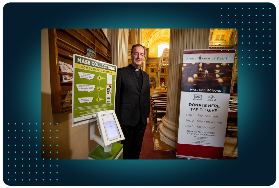 Priest beside an Archdiocese of Dublin mass collections donation kiosk in a church